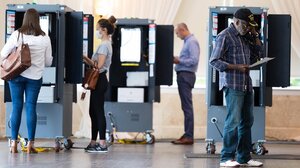 Four people standing near voting machines, either about to or currently submitting their votes