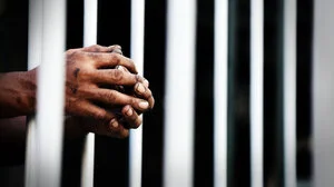 Prisoner's clasped hands resting on jail bars
