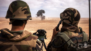 Two soldiers watch a distant explosion in the desert