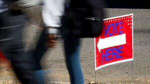 People walking past a vote here sign with an arrow