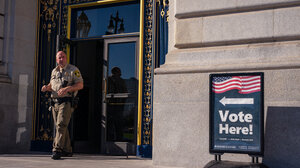 law enforcement officer outside polling place, near vote here sign