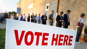 People in line to vote in background with Vote Here sign in foreground